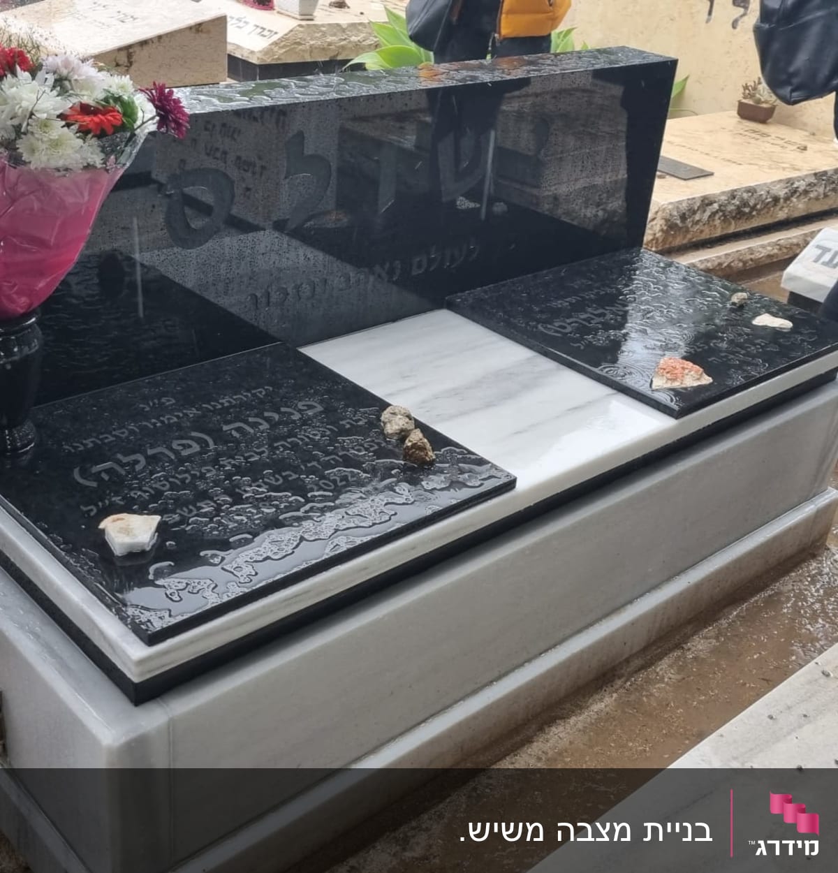 מצבה שחורה עם כיתוב ופרחים באגרטל